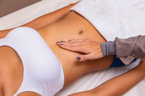 a woman wearing a white bra and towel on her abdomen receiving a modelling massage 